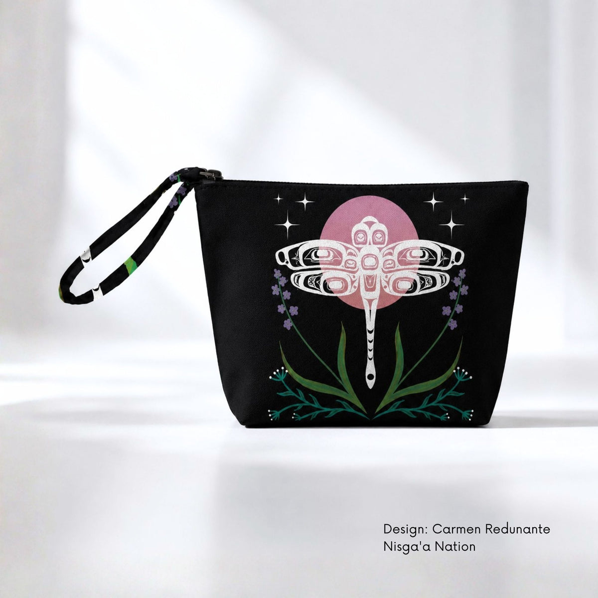 Black canvas pouch featuring a white dragonfly in front of a pink moon, surrounded by stars, purple flowers and green plants.