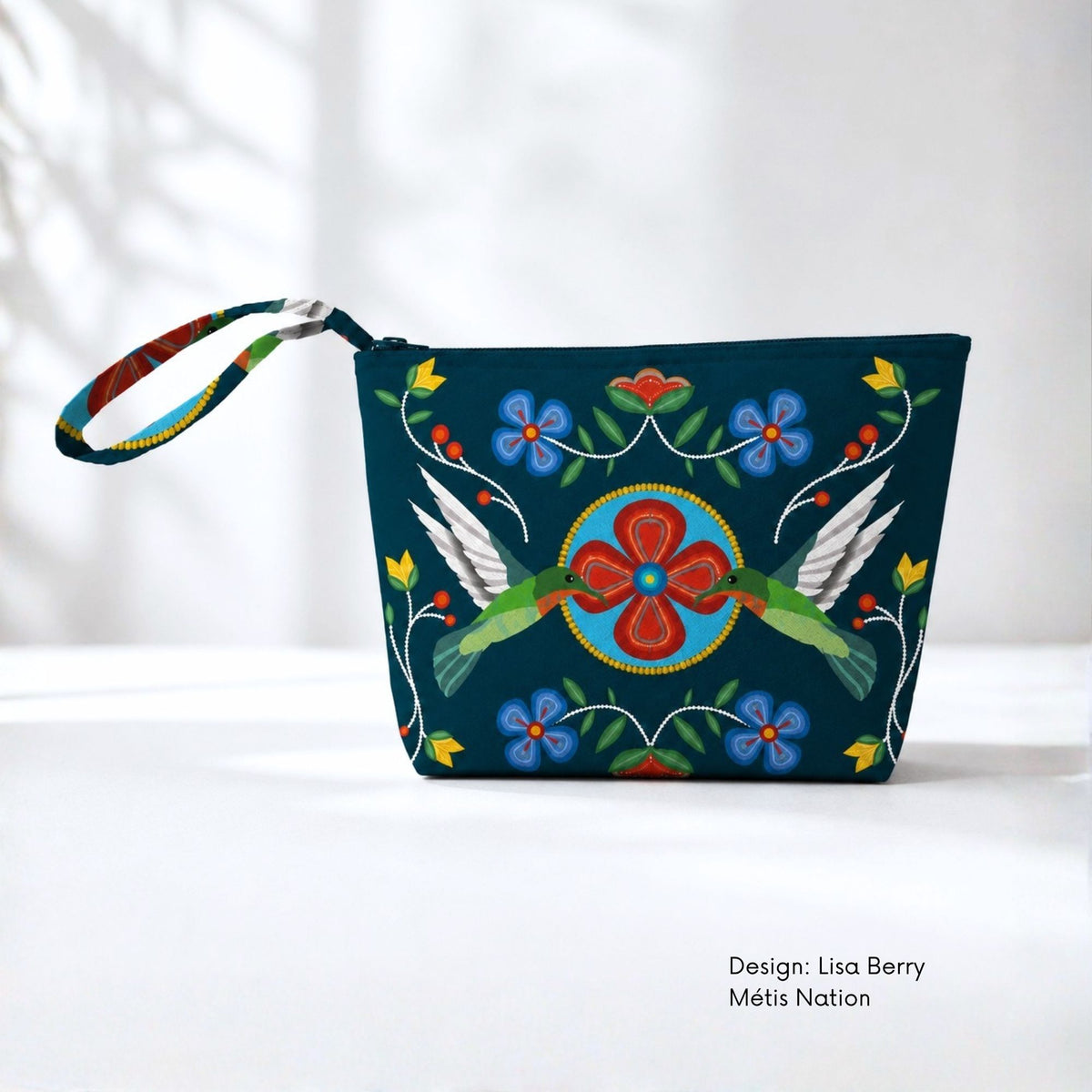 Dark teal canvas pouch featuring two green hummingbirds facing a central red flower, surrounded by blue flowers, green leaves, buds and dotted white stems.