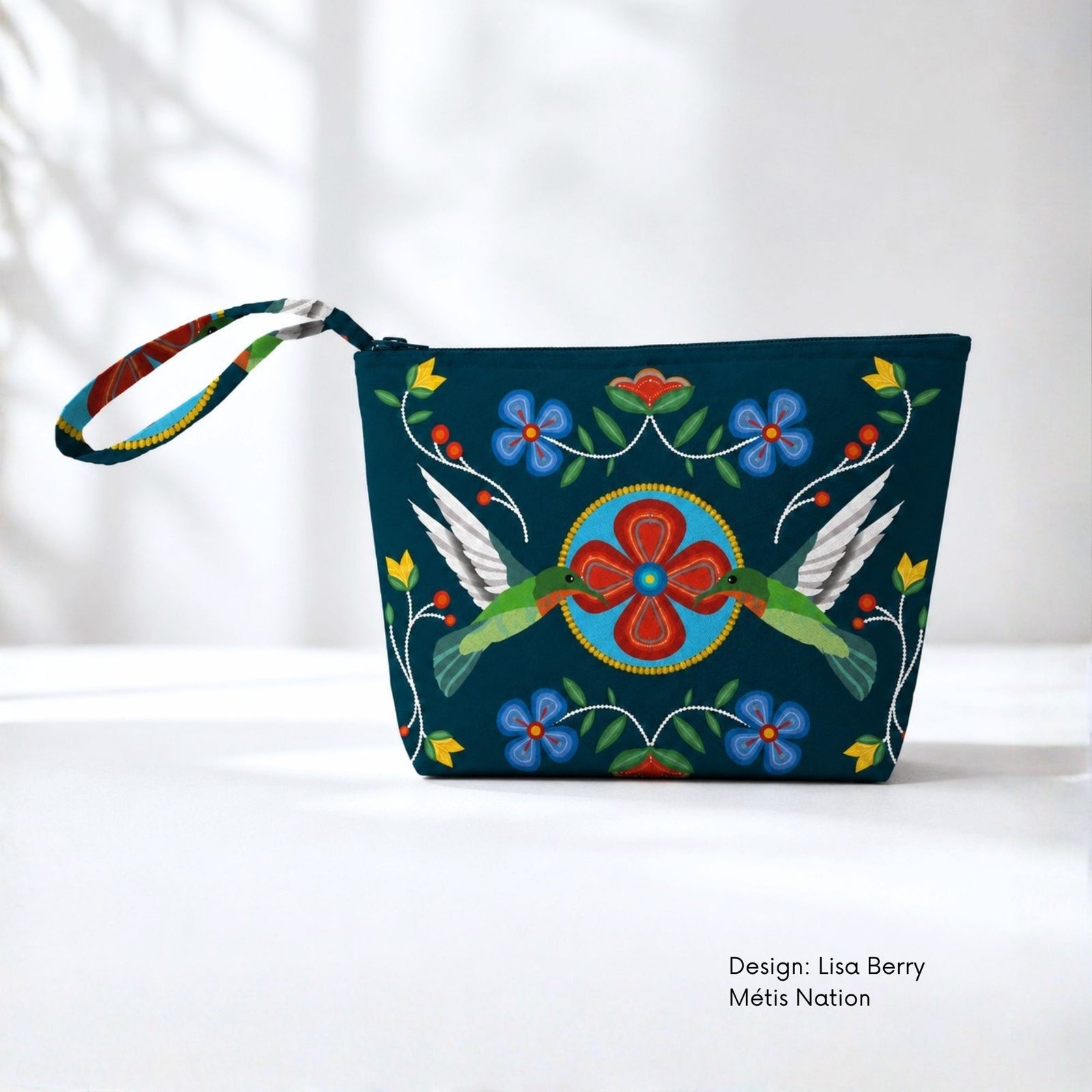 Dark teal canvas pouch featuring two green hummingbirds facing a central red flower, surrounded by blue flowers, green leaves, buds and dotted white stems.