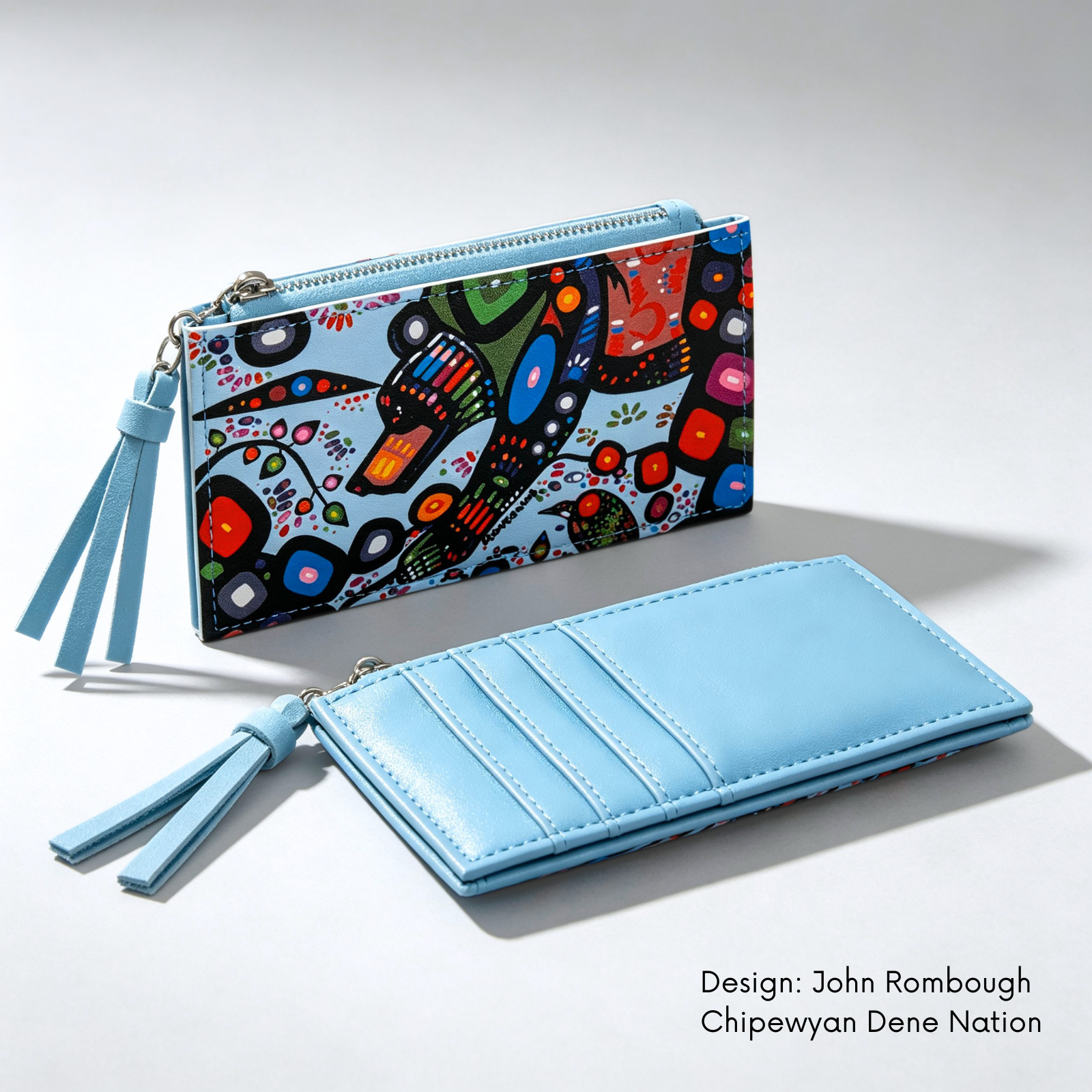 A light blue zip-around wallet shown in two views on a white studio background. One view shows John Rombough’s colourful Bear artwork, with tassel pull, and the other shows the interior card slots and tassel.

