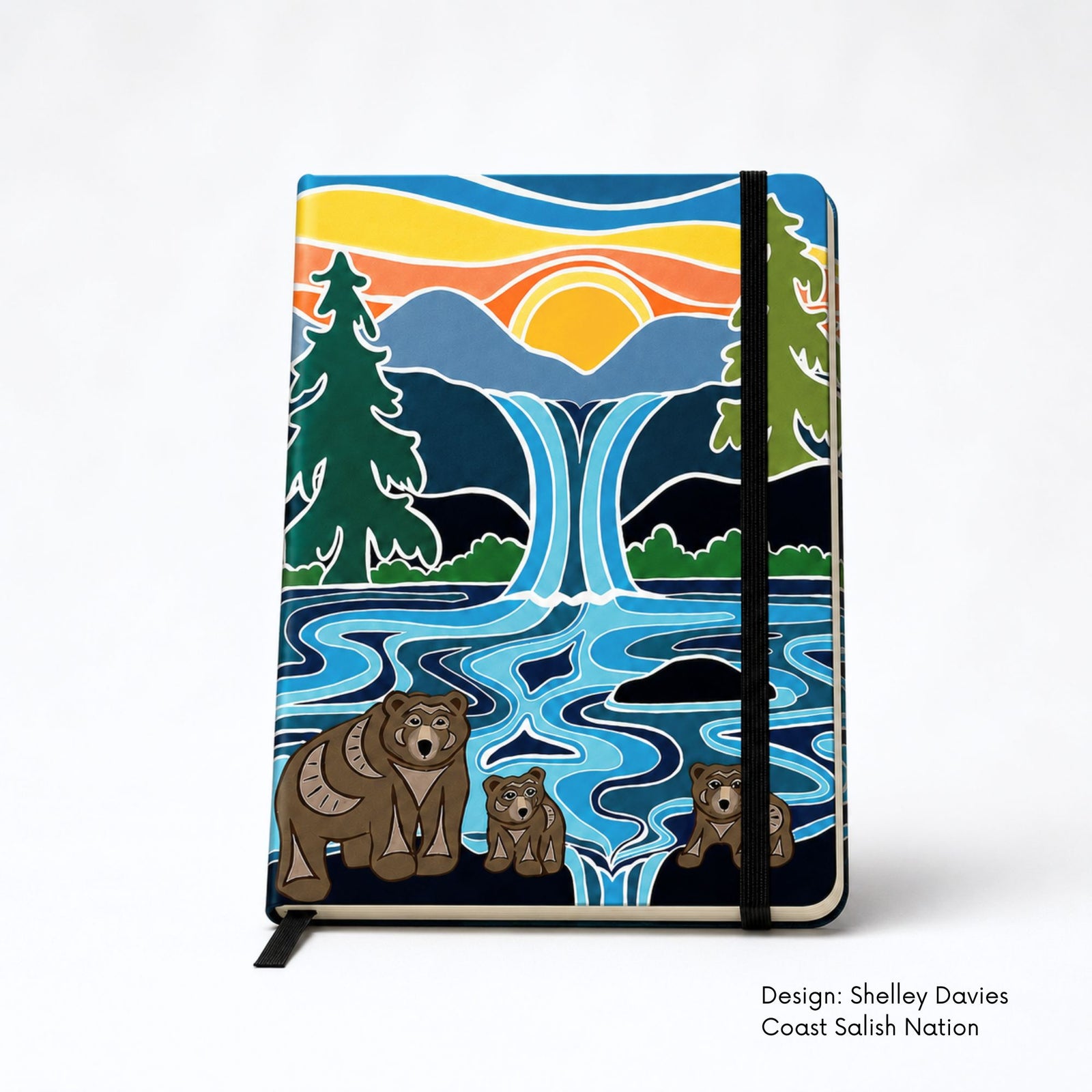 Hand holding Hardcover journal featuring Shelley Davies’ One Last Swim, with three bears beside a flowing river and waterfall beneath mountains and a setting sun.
