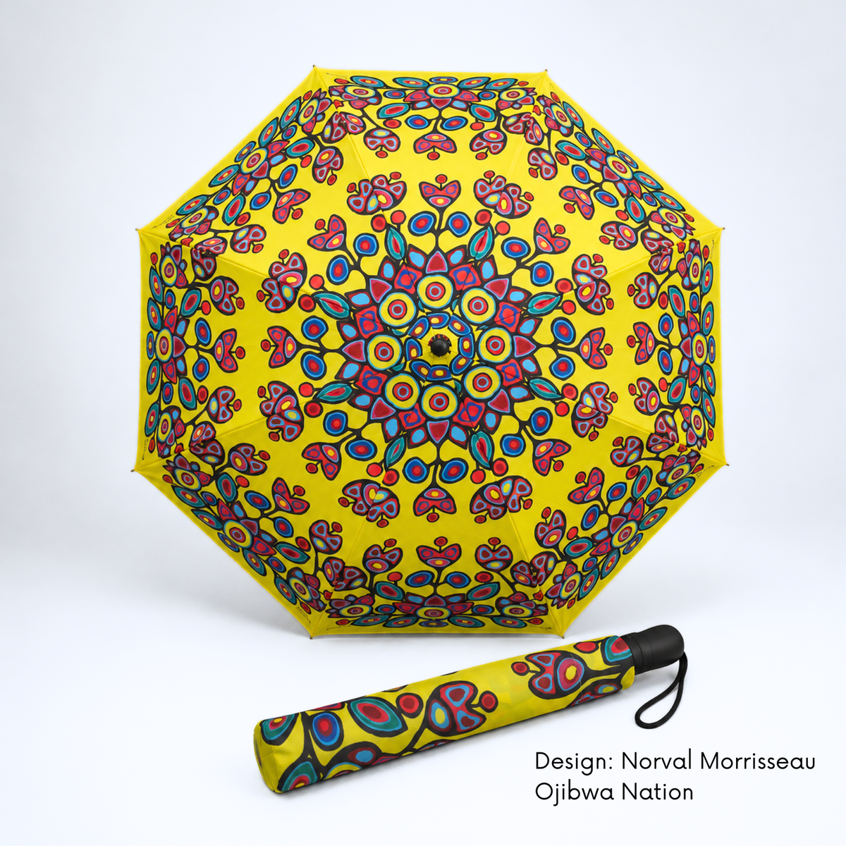 A bright yellow folding umbrella featuring Norval Morrisseau’s colourful Floral on Yellow artwork shown open with its matching folded version below on a white studio background. Text at the bottom right reads 'Design: Norval Morrisseau Ojibwa Nation'.