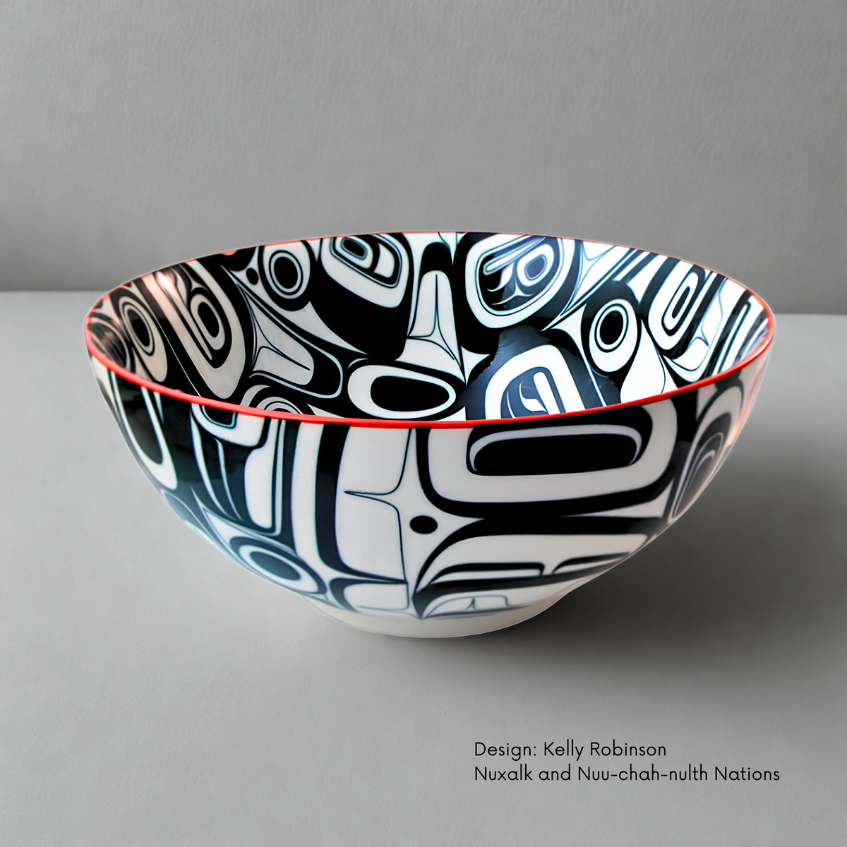 Large porcelain bowl featuring Raven Transforming artwork by Nuxalk and Nuu-chah-nulth artist Kelly Robinson, with bold black and white forms and a red rim.