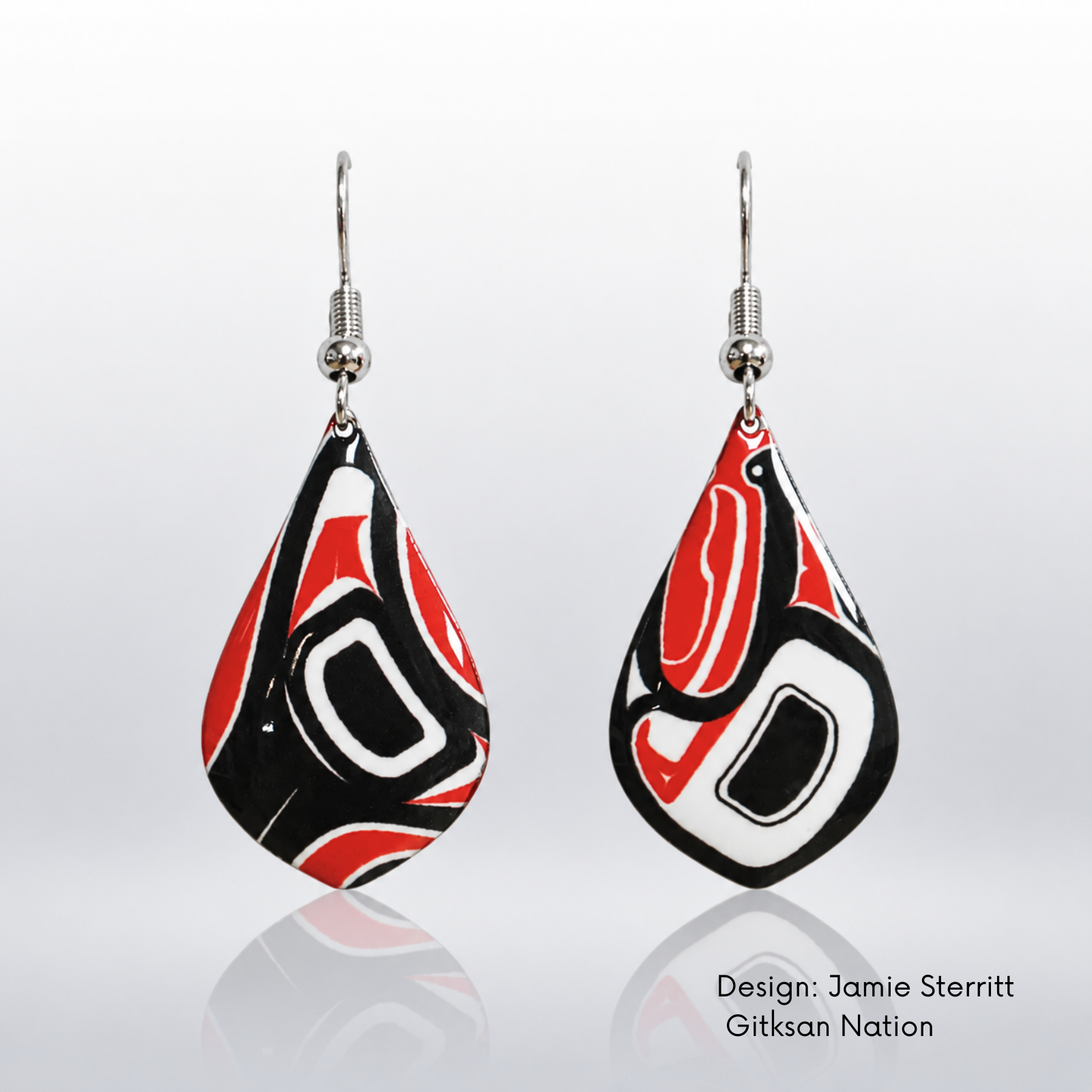 A pair of teardrop-shaped dangle earrings with a Gitxsan Nation design by Jamie Sterritt. The earrings feature a bold, abstract pattern in red, black, and white, suspended from silver fishhook wires.