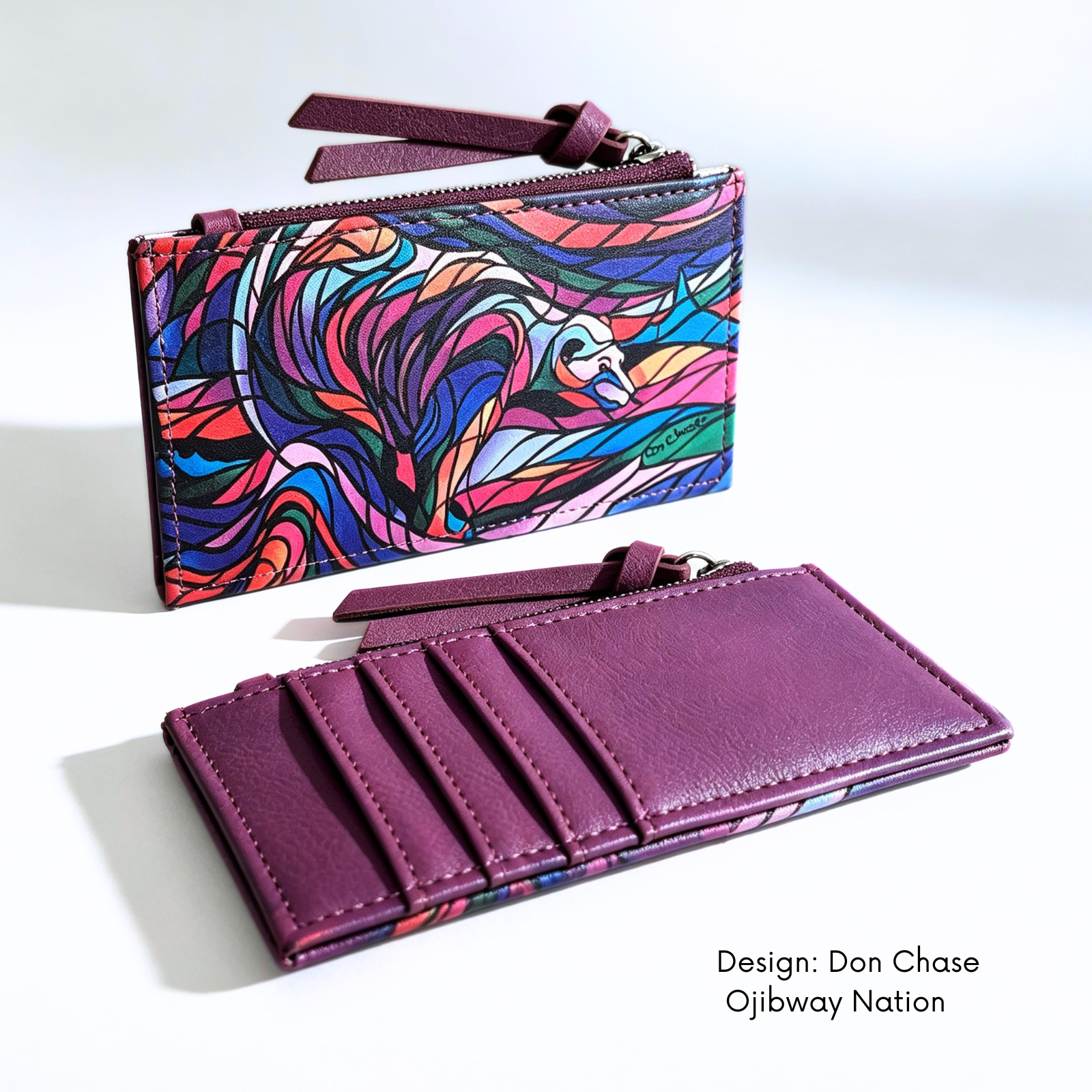 Plum synthetic leather card holder featuring Don Chase’s colourful Salmon Hunter artwork.


A purple zip-around wallet shown in two views on a white background: one closed with a colorful abstract wave design and one open showing card slots and a wrist strap. Text at bottom right reads 'Design: Don Chase Ojibway Nation'.